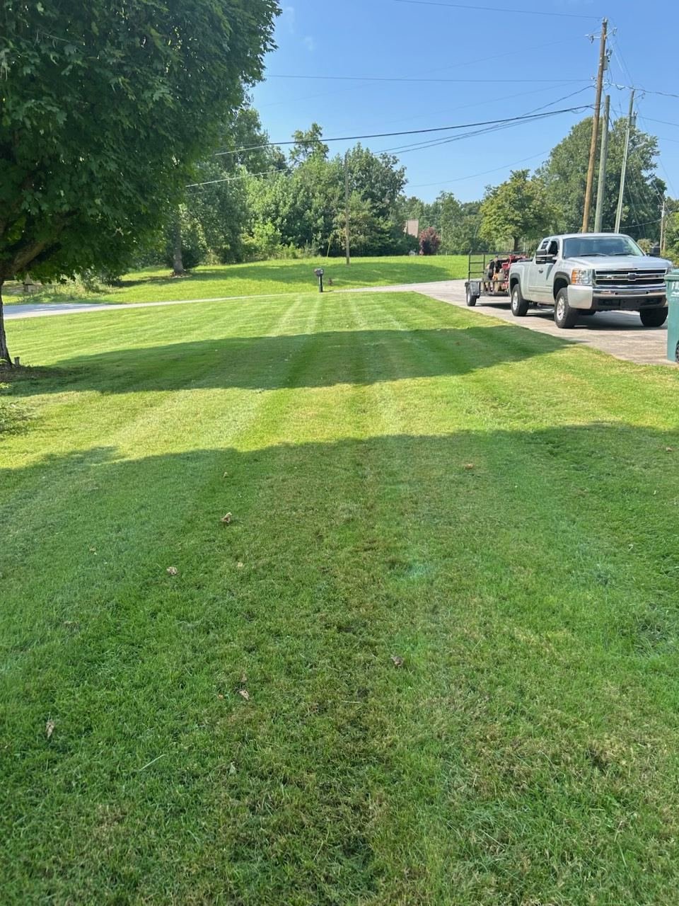 Quality Lawn & Landscape work truck and trailer loaded with equipment beside a freshly striped lawn in Wilkes County, NC